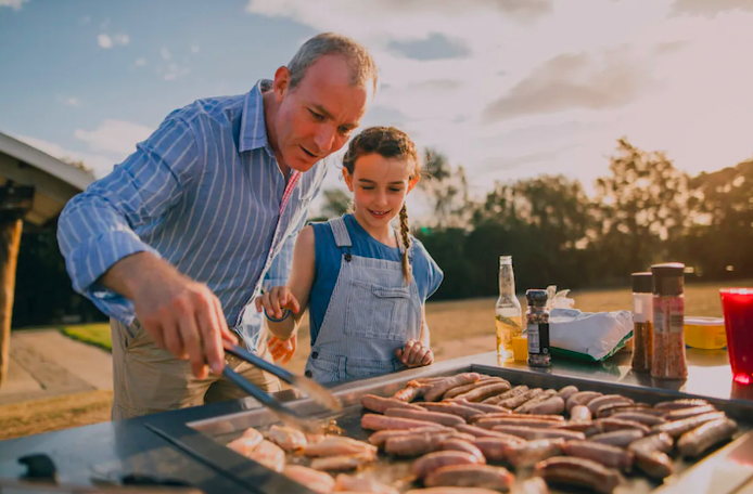 a photo of a dad and daughter cooking on a grill outside