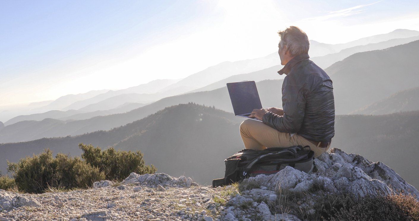 a man sitting outside with his computer looking at the mountains.