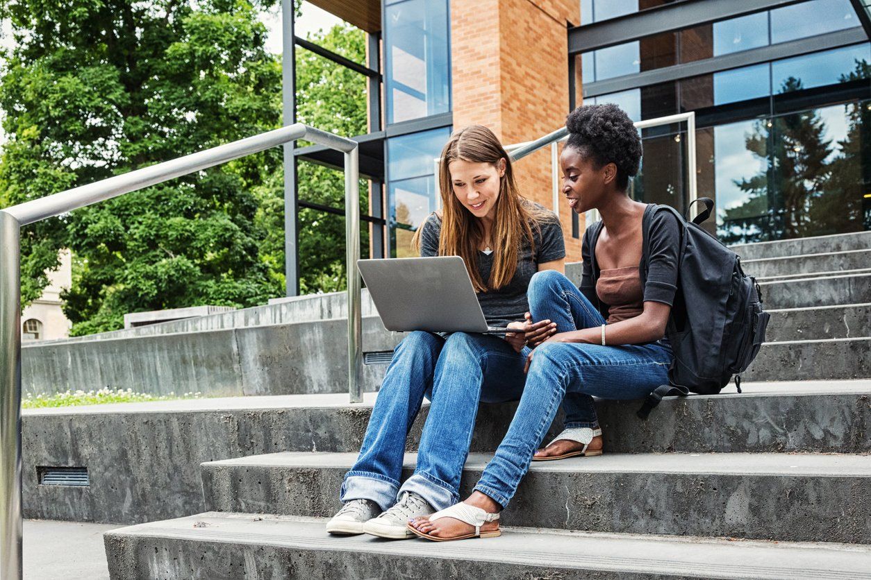 a photo of two female college students talking on the steps of their campus