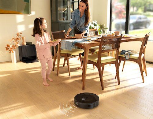 a photo of a woman and child in the dinning room with iRobot's Roomba Combo 10 Max Robot + AutoWash Dock vacuuming the floor