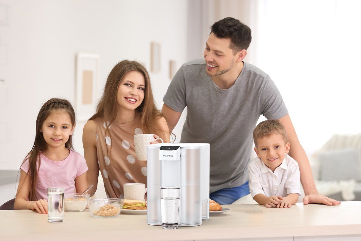 a photo of a family around a counter with the Waterdrop Mega Electric Water Filter Pitcher and glasses of water