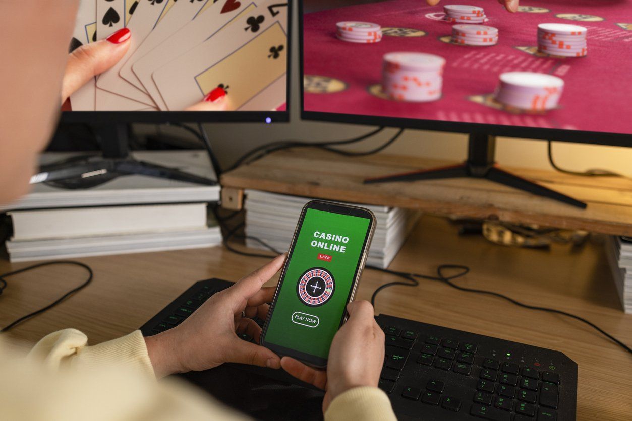 a person playing online casino game on his smartphone with computer screens showing online gaming.