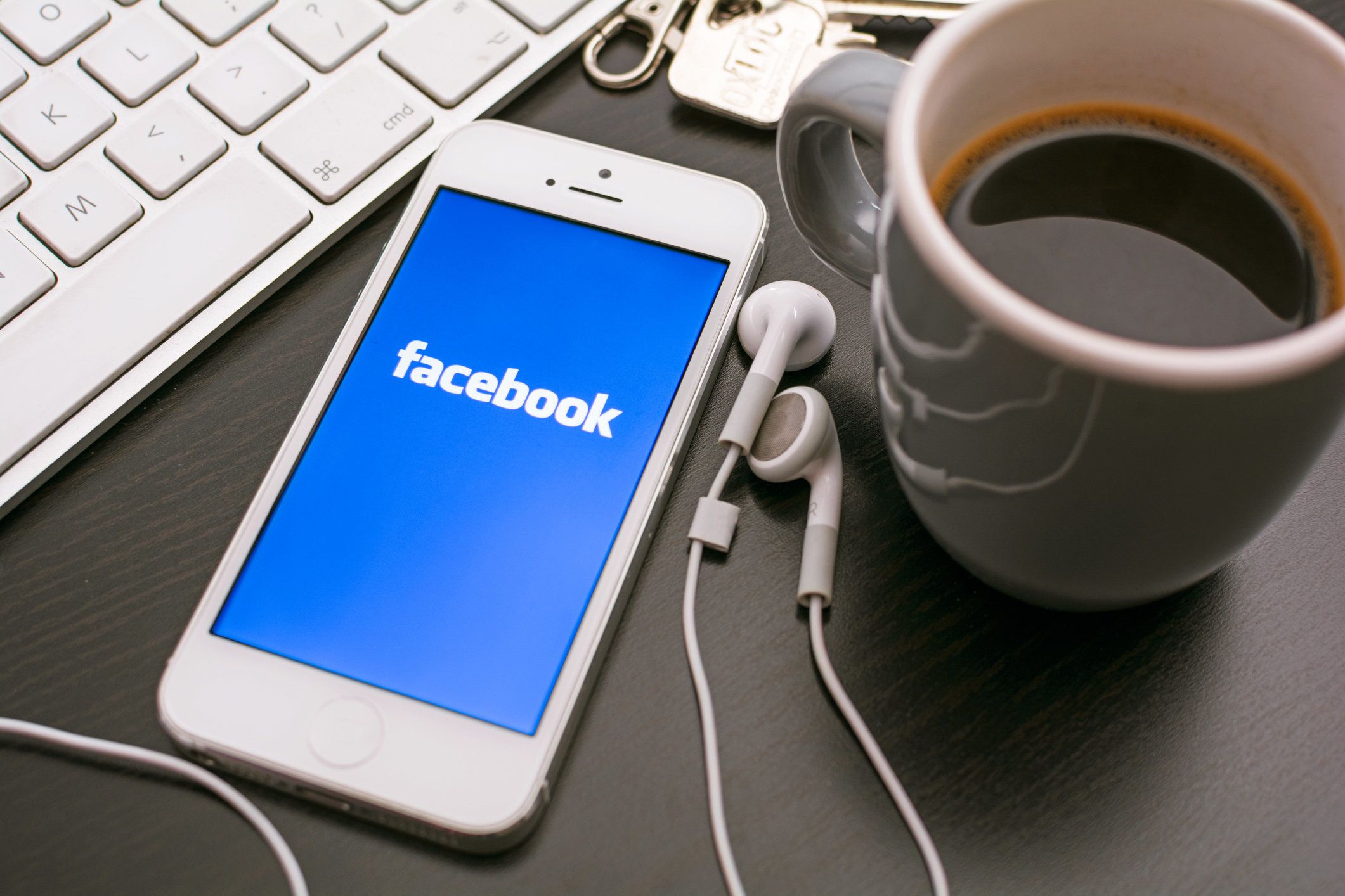 photo of smartphone on desk next to laptop with Facebook logo on its screen