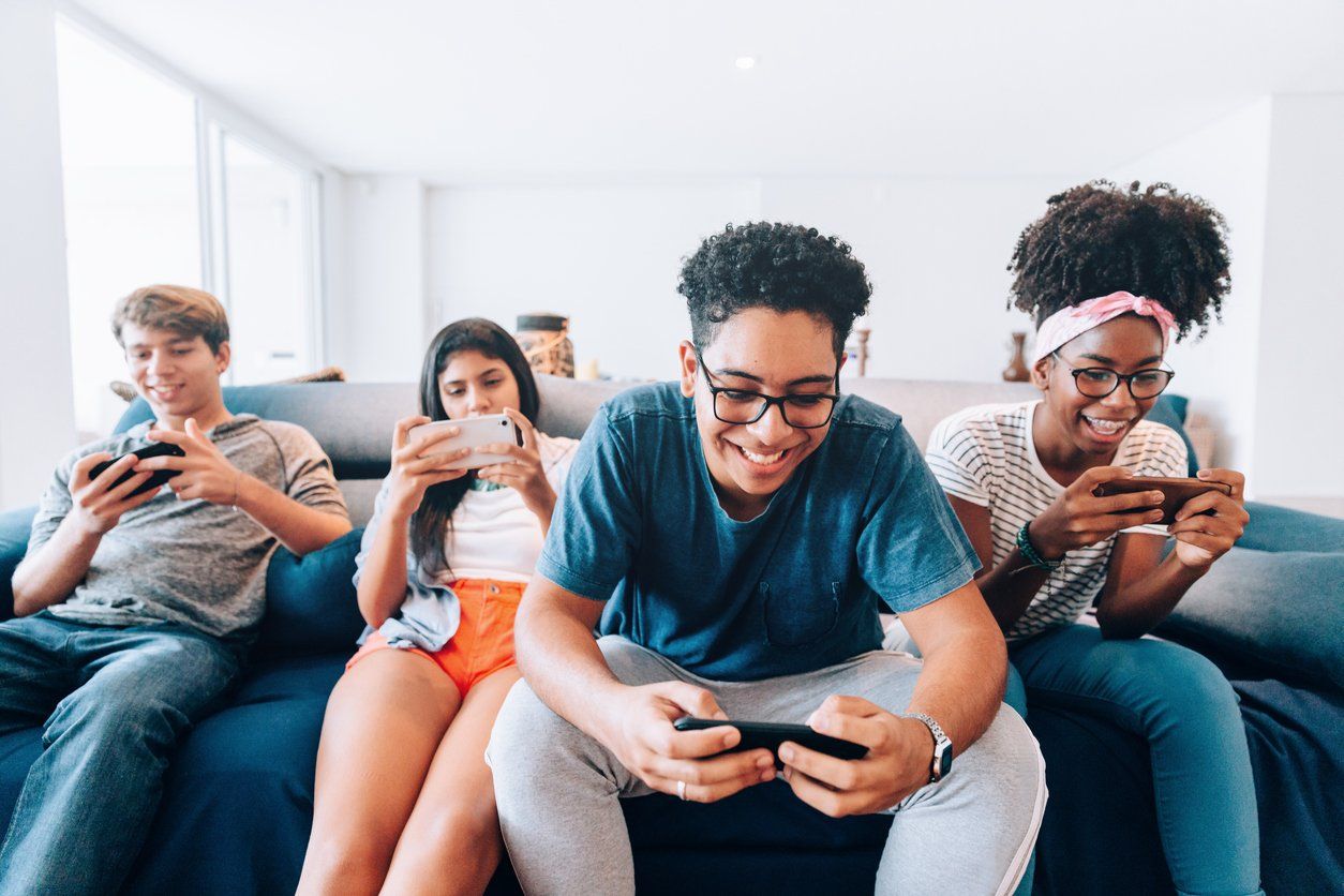 a photo of young adults playing games on their smartphones while sitting on a couch.