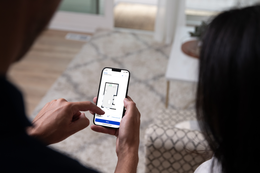 a photo of a person on their smartphone using MyLowe's Home app to create a map of their kitchen.
