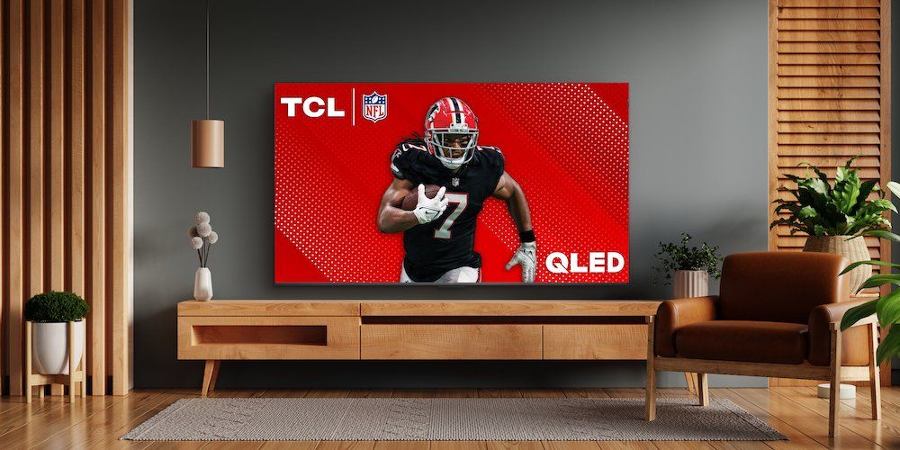 a photo of TCL 115" Q Class QM89 Smart TV in a living room on a stand with a football player running.